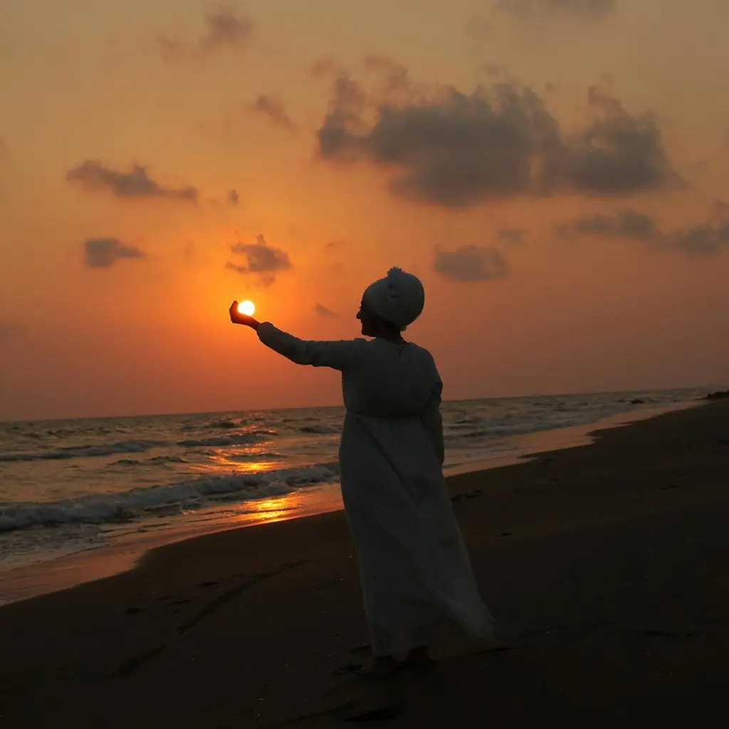 Mulher na praia ao entardecer segurando o sol.